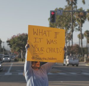 Eine Frau hält ein gelbes Schild hoch, auf der steht: What if it was your child?