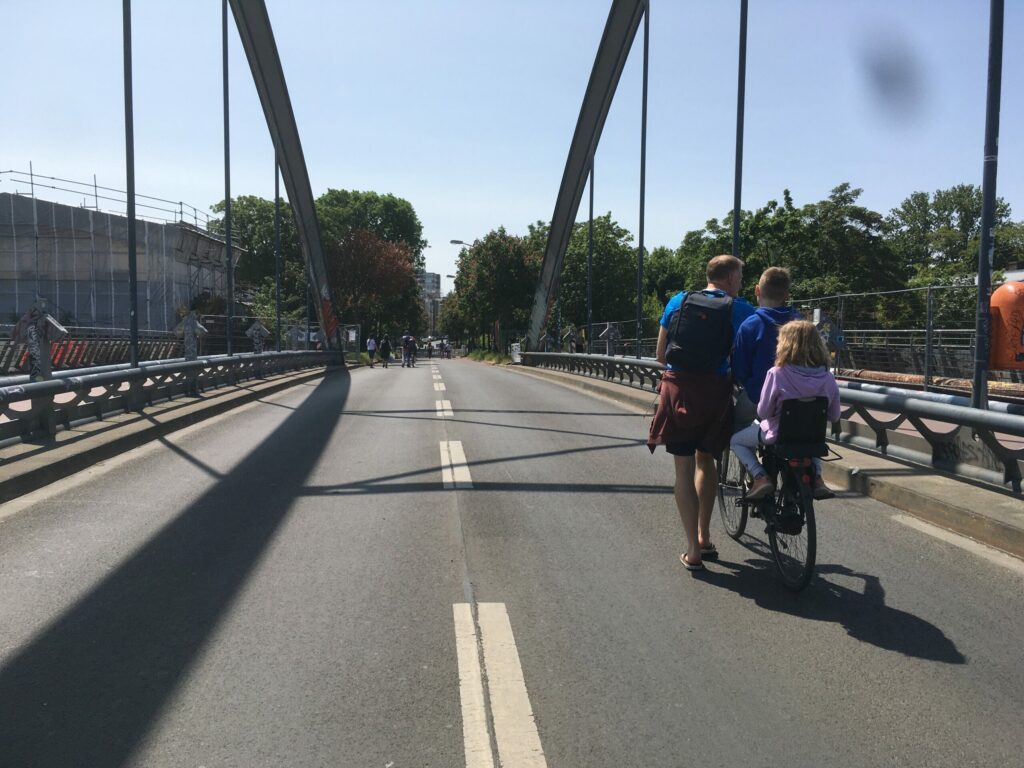 Für den Autoverkehr gesperrte Modersohnbrücke: AUf der Fahrbahn ein Erwachsener, der ein Rad schiebt, auf dem zwei Kinder sitzen.