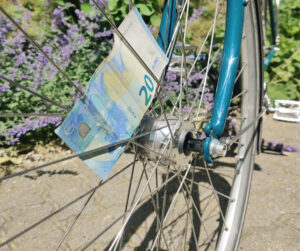 Foto eines Fahrrades. Es ist hauptsächlich das Vorderrad zu sehen, zwischen den Speichen steckt ein 20-Euro Schein.