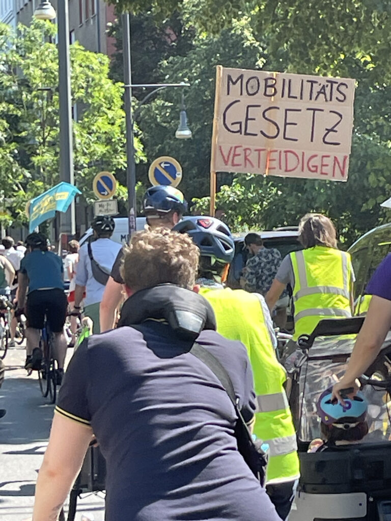 Eine Raddemo: Jemand aht ein selbstgemaltes Schild: Mobilitätsgesetz verteidigen