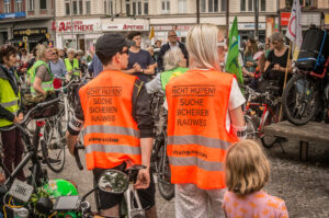 Zwei Menschen tragen Warnwesten bei einer Demonstration: NIcht hupen, suche sicheren Radweg, Changing Cities