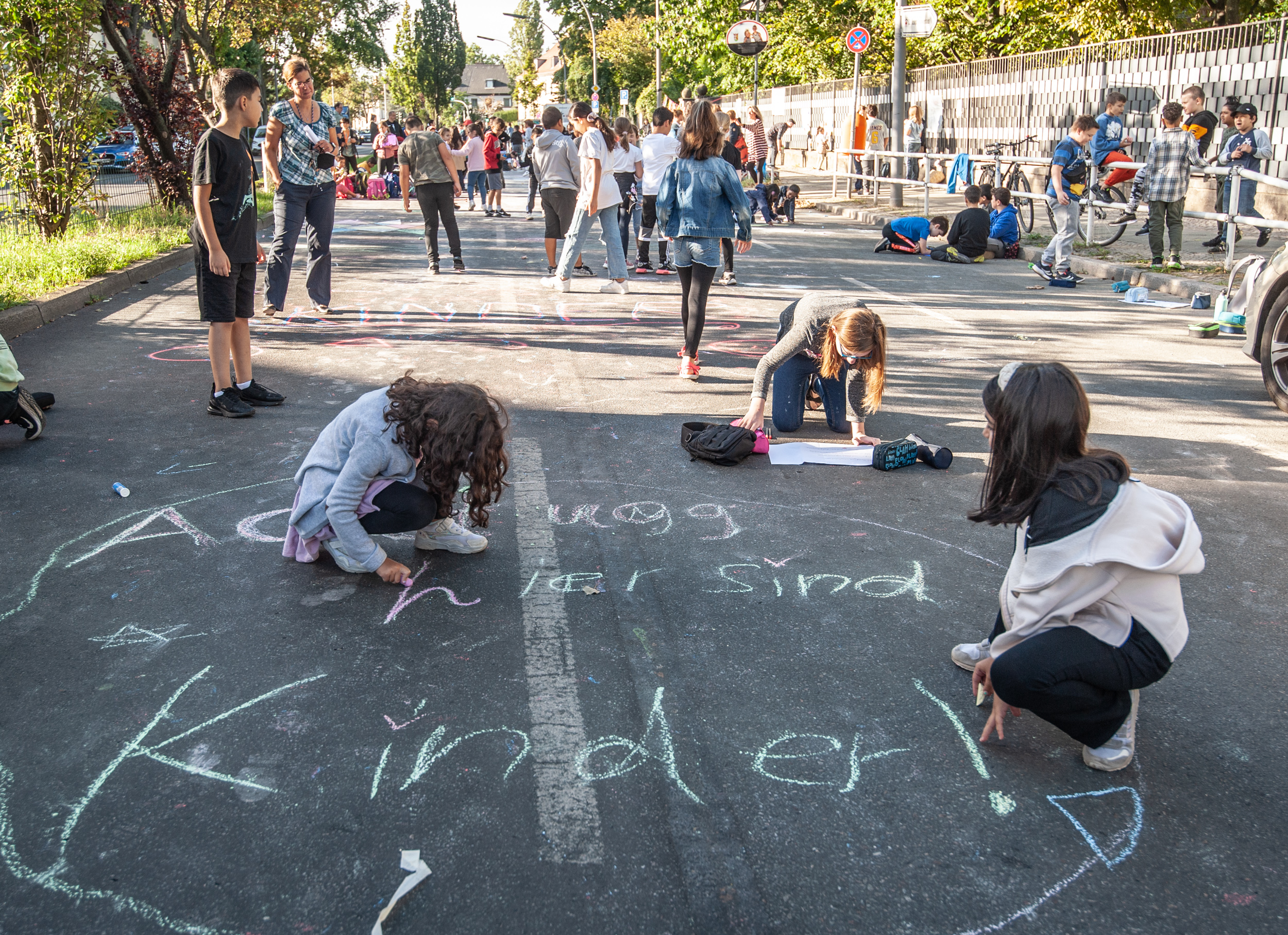 Kinder malen auf einer Straße, die von Autos befreit ist: eine Schulzone.