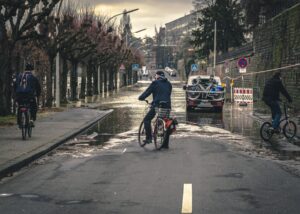 Ein Radfahrer steht vor einer überschwemmten Straße, die unpassierbar ist.