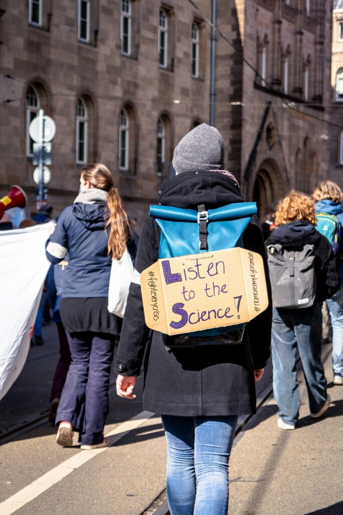 Eine person auf eine Demo trägt ein selbst gemaltes Schild: Listen to the science.