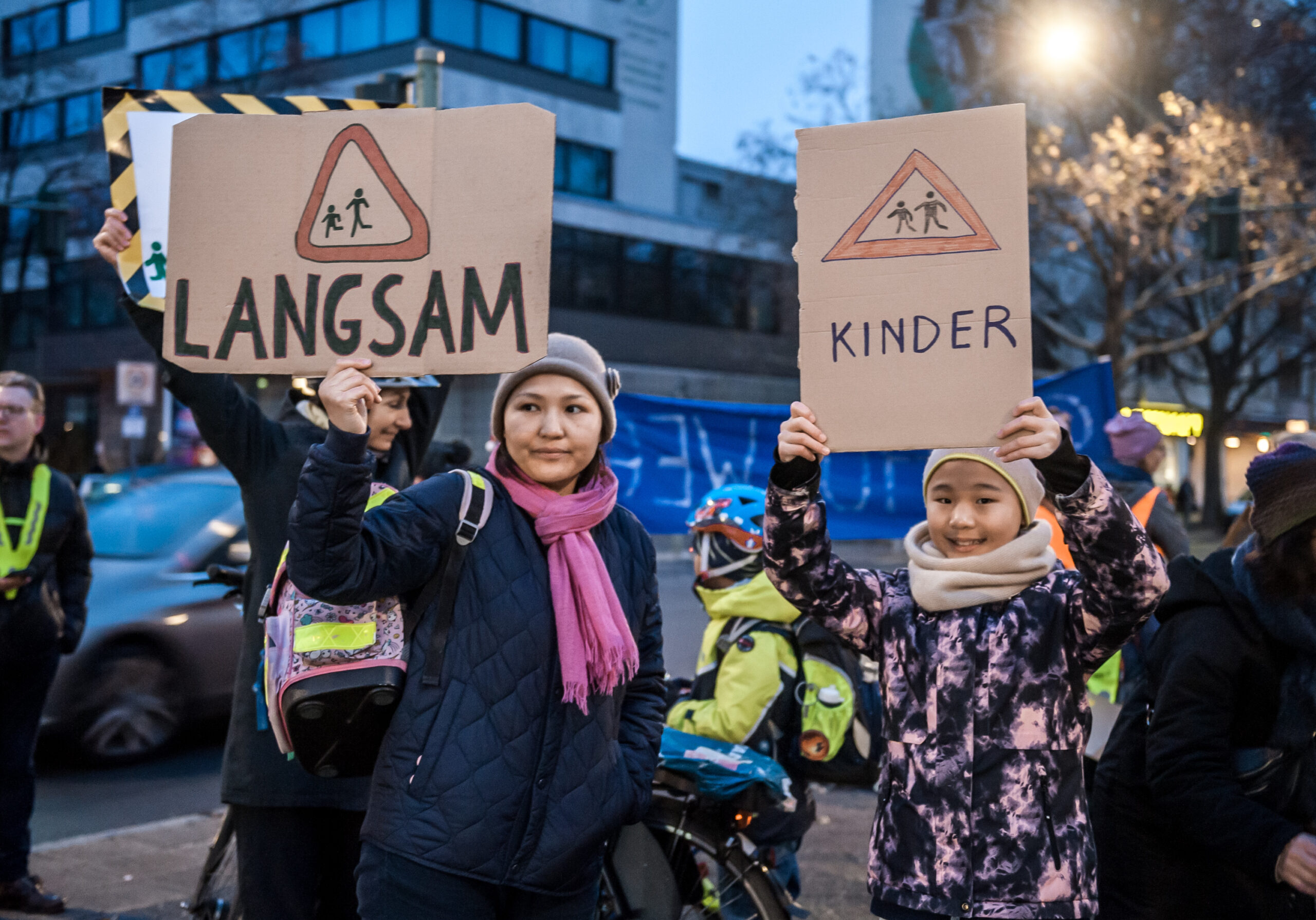 Mutter und Kind demonstrieren für Schulwegsicherheit mit Pappschildern: Langsam, Kinder