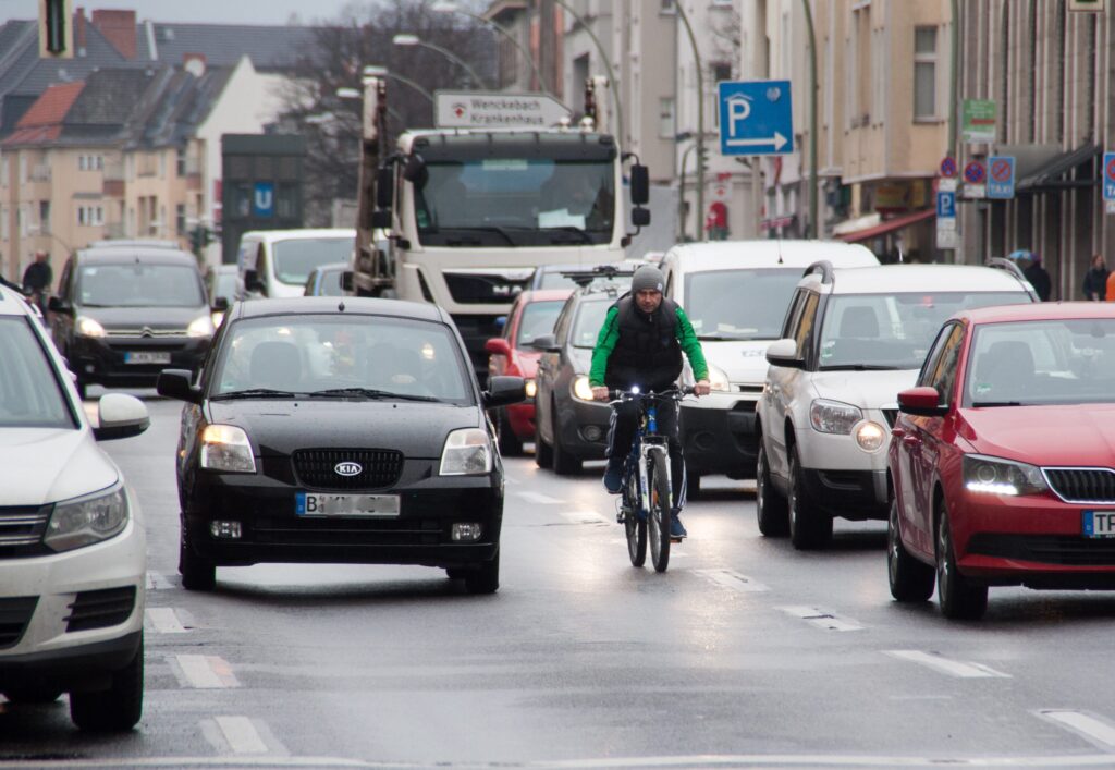 Radfahrer fährt zwischen dichtem Autoverkehr auf einer nassen Stadtstraße