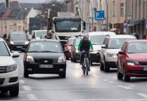 Radfahrer fährt zwischen dichtem Autoverkehr auf einer nassen Stadtstraße