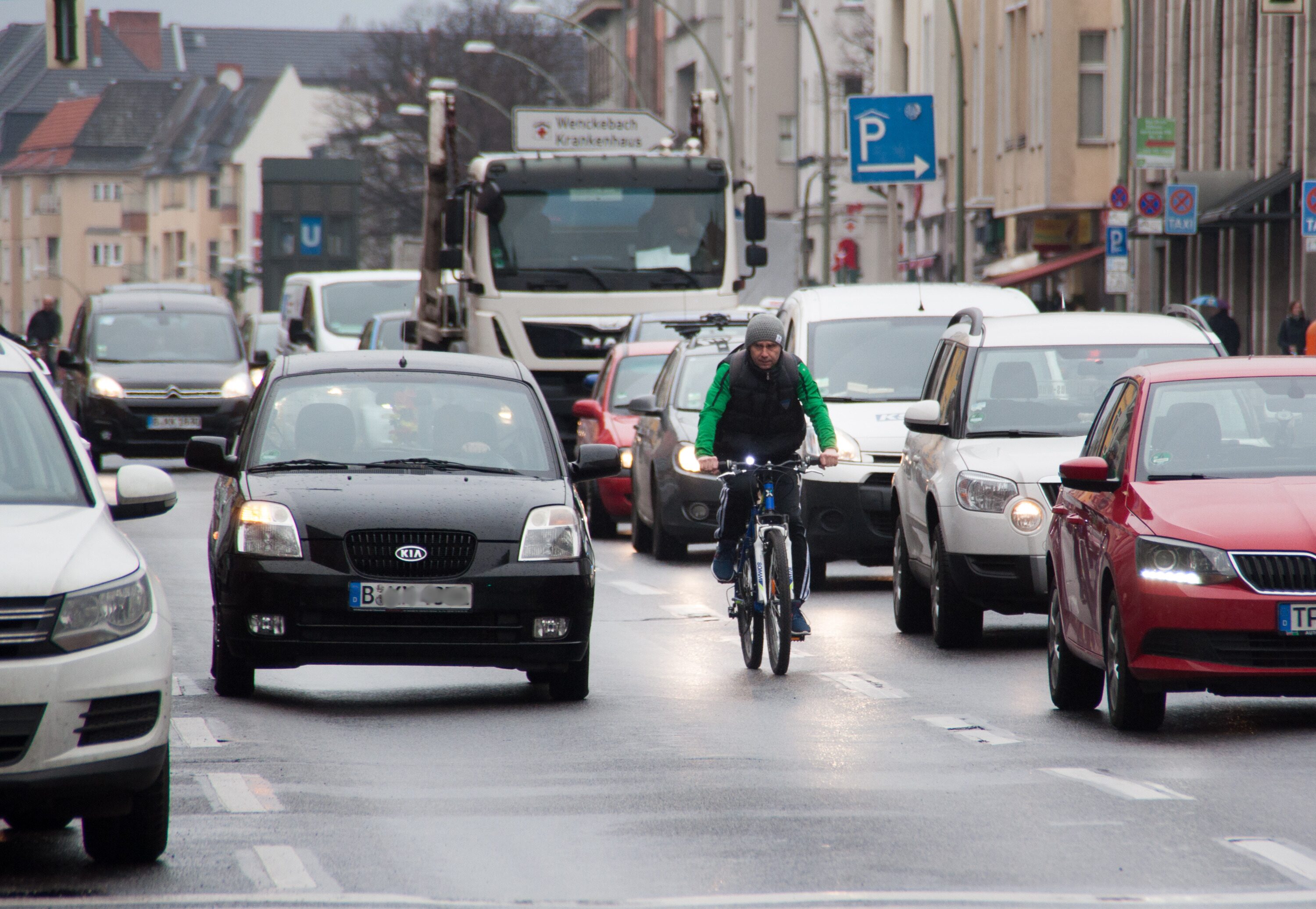 Radfahrer fährt zwischen dichtem Autoverkehr auf einer nassen Stadtstraße