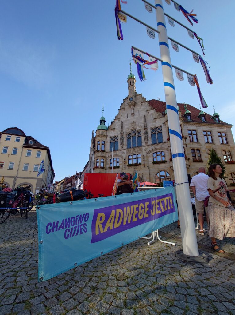 Stadtplatz mit Fahrraddemo; Banner „CHANGING CITIES“ und „RADWEGE JETZT!“ vor historischem Rathaus