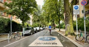 Fahrradstraße mit Radfahrerin, parkenden Autos und Beschilderung „Anlieger frei“