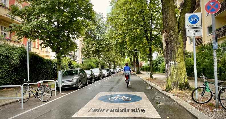 Fahrradstraße mit Radfahrerin, parkenden Autos und Beschilderung „Anlieger frei“