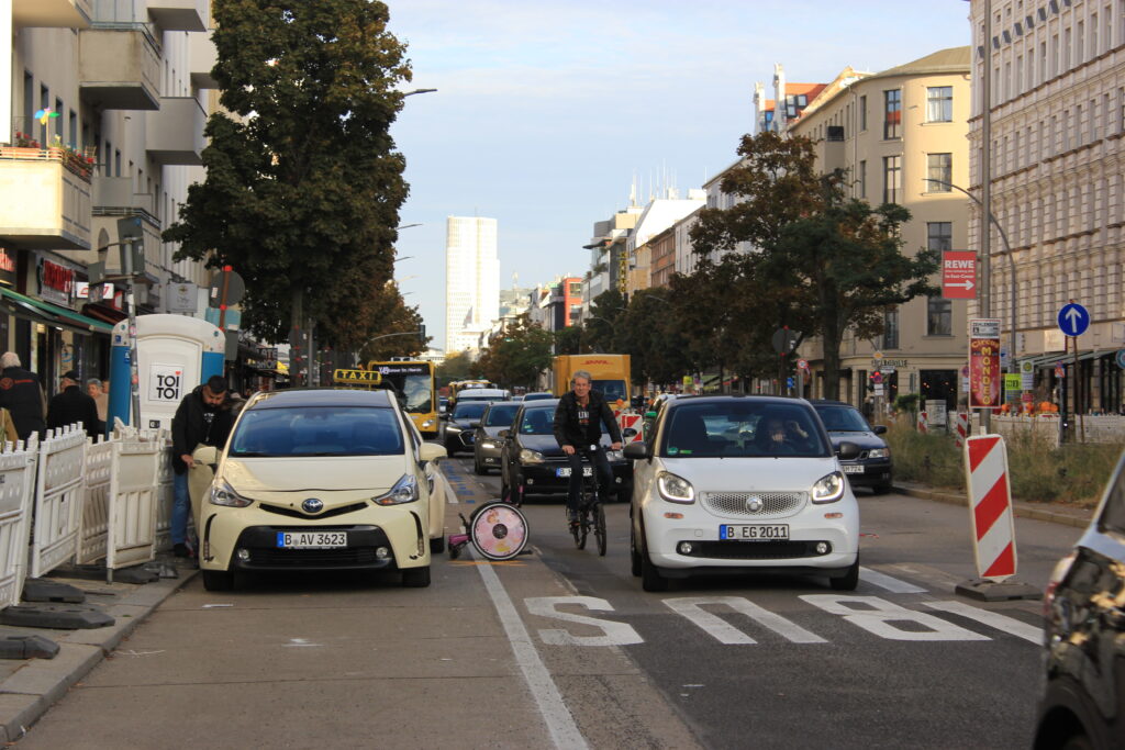 Starker Stadtverkehr auf einer Berliner Straße mit Autos, Radfahrer und Lieferwagen zwischen Wohnhäusern
